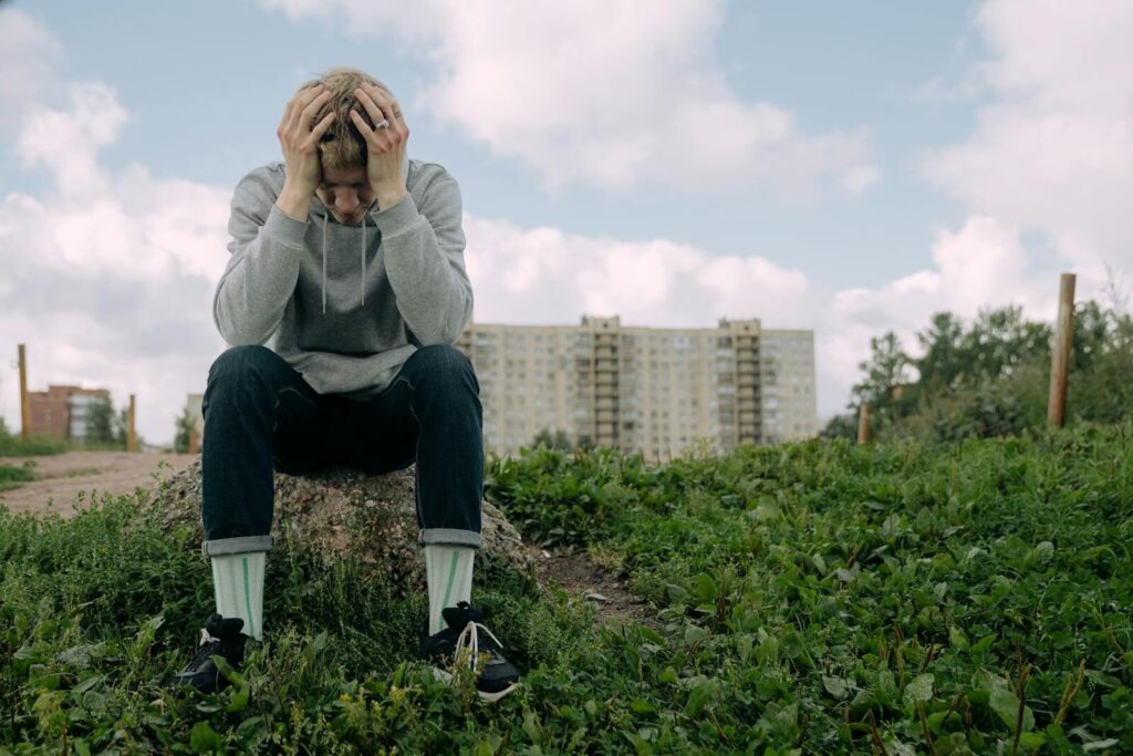 A man sitting with head in hands outdoors, showing stress and contemplation.