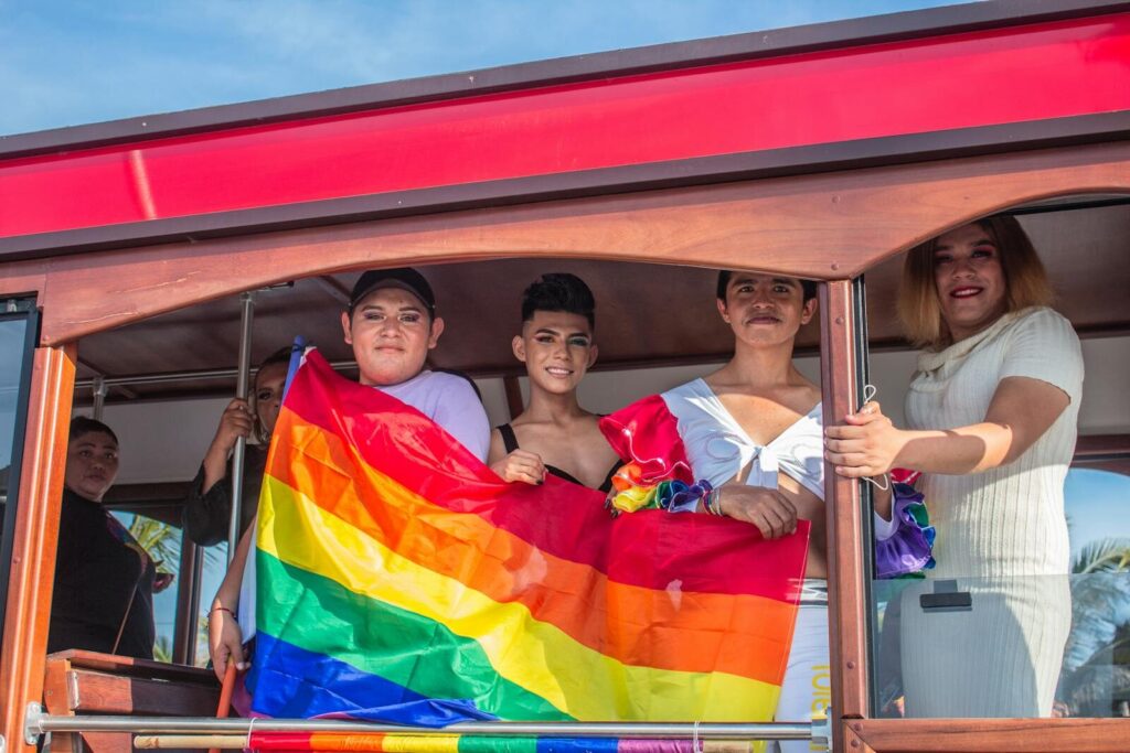 Cheerful group celebrating Pride with a rainbow flag on a bus. Vibrant and joyful atmosphere.